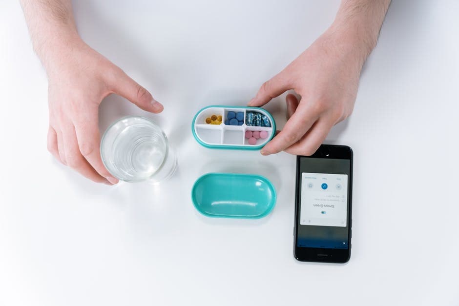 Overhead view of hands using a smartphone app and pill organizer for medication management