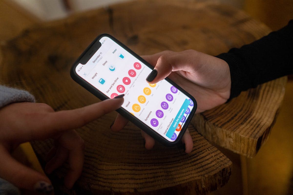 A person using a smartphone app to log health data, with a lab results printout next to them on a desk