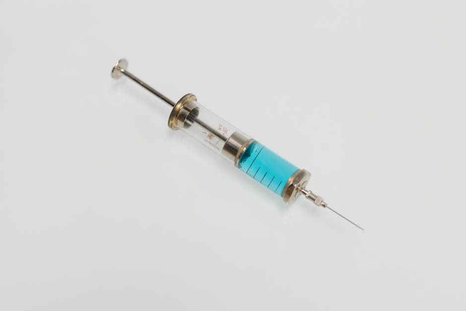 A clean countertop with a testosterone vial, syringe, alcohol swabs, and a sharps container set out for an injection