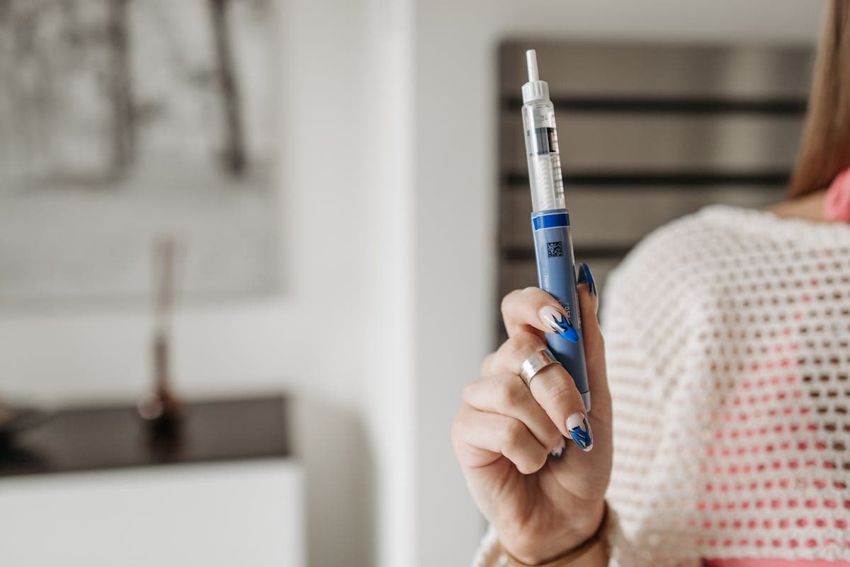 A person's hands holding a Mounjaro pen against their abdomen, demonstrating the flat base placement technique