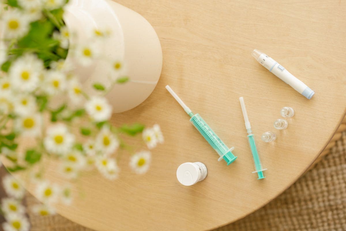A person's hands laying out an injection pen, alcohol swab, and pen needle on a clean white countertop in preparation for a subcutaneous injection