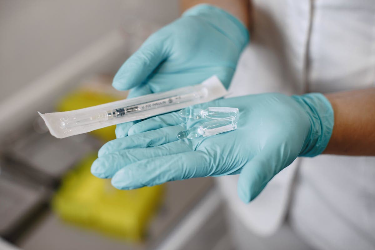 Person preparing a subcutaneous injection with an insulin syringe and a small vial of testosterone on a clean countertop
