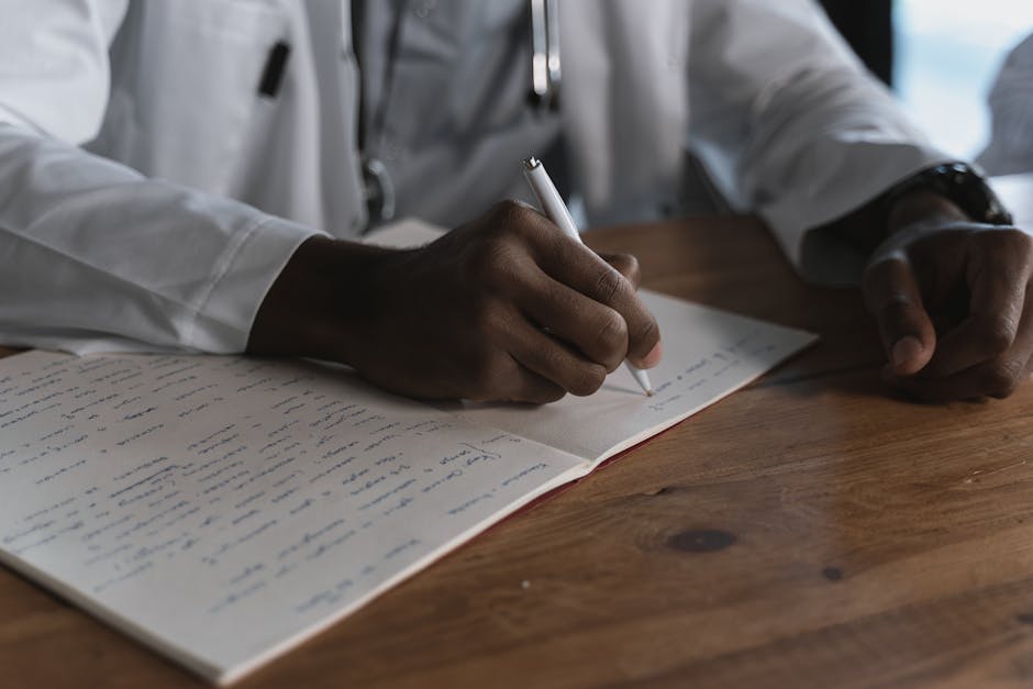 Close-up of a doctor writing notes with a pen in a medical notebook on a wooden desk